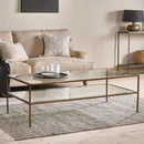 Rectangular glass coffee table with brass legs and a glass shelf styled in a living room with Scandi influences