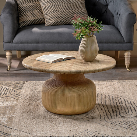 Round mango wood coffee table with grooved texture in a living room