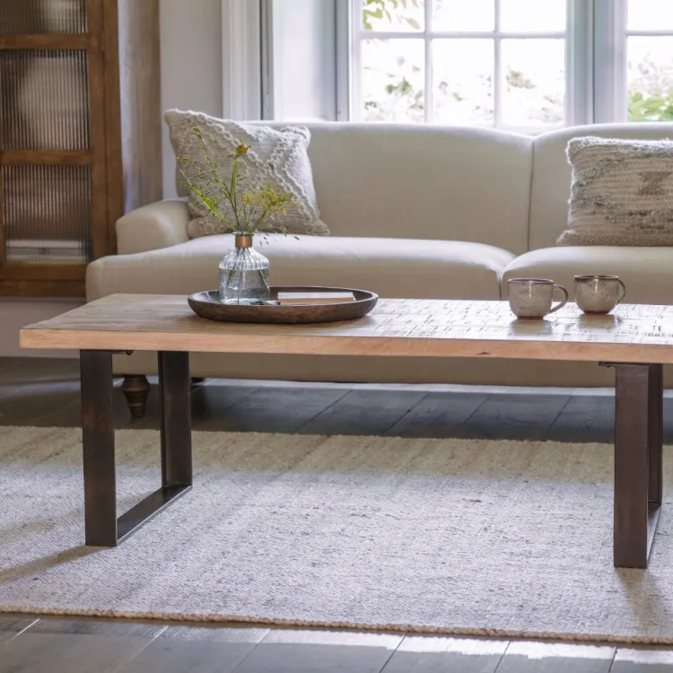 A wooden coffee table on top of a rug and by a sofa